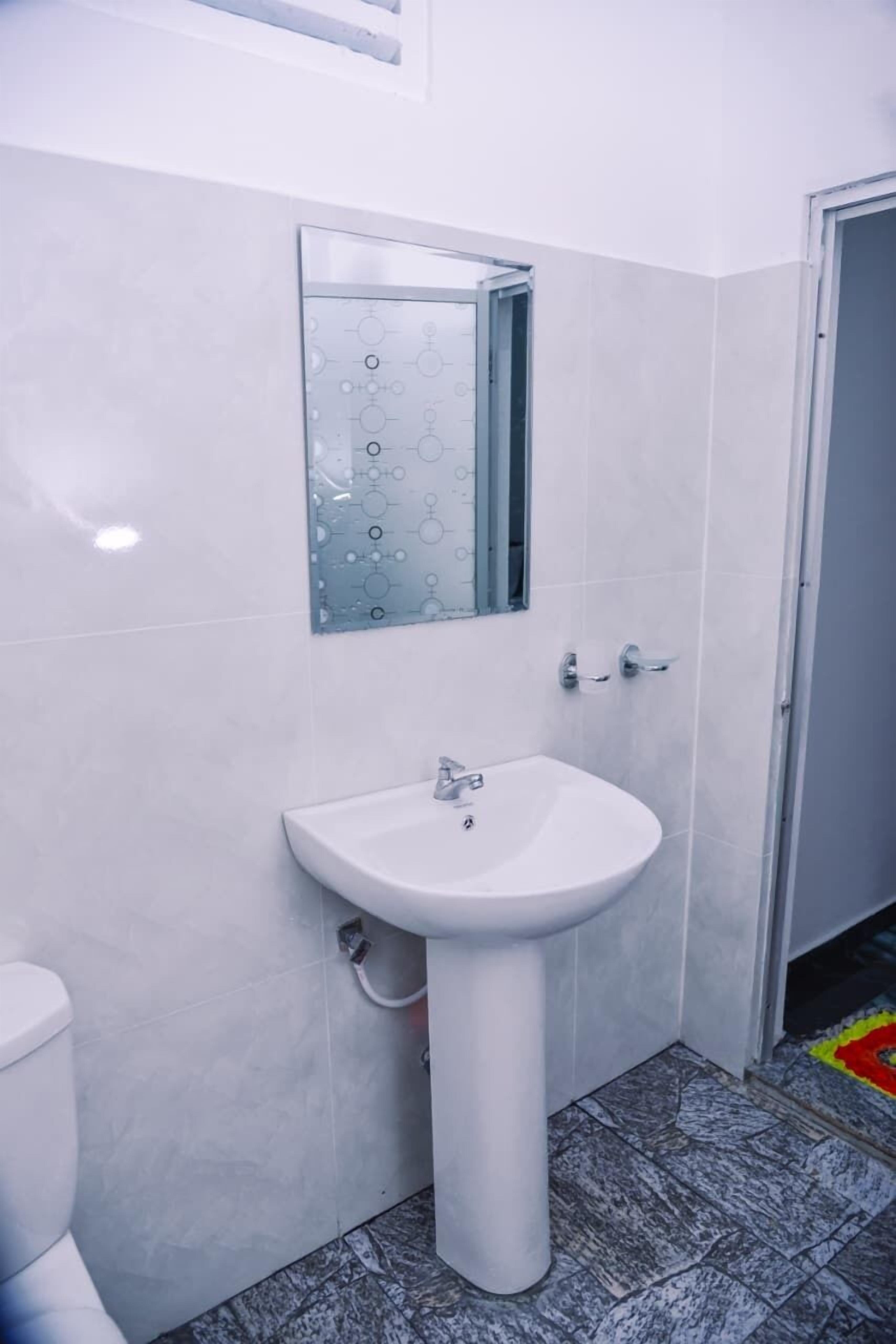 Un baño con un lavamanos pedestal blanco, un espejo encima y un inodoro a la izquierda.