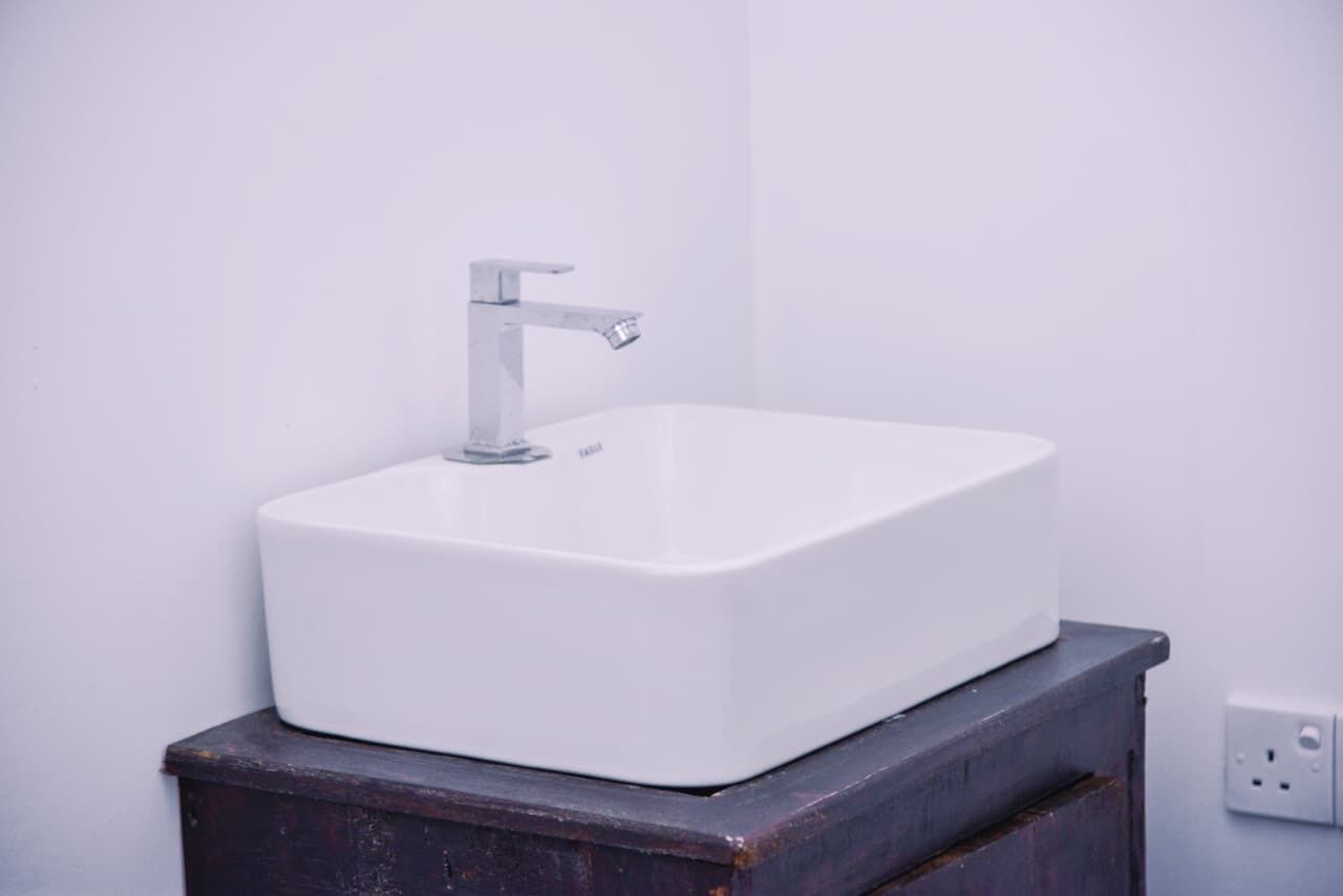 A white rectangular bathroom sink on a dark wooden cabinet against a white wall.