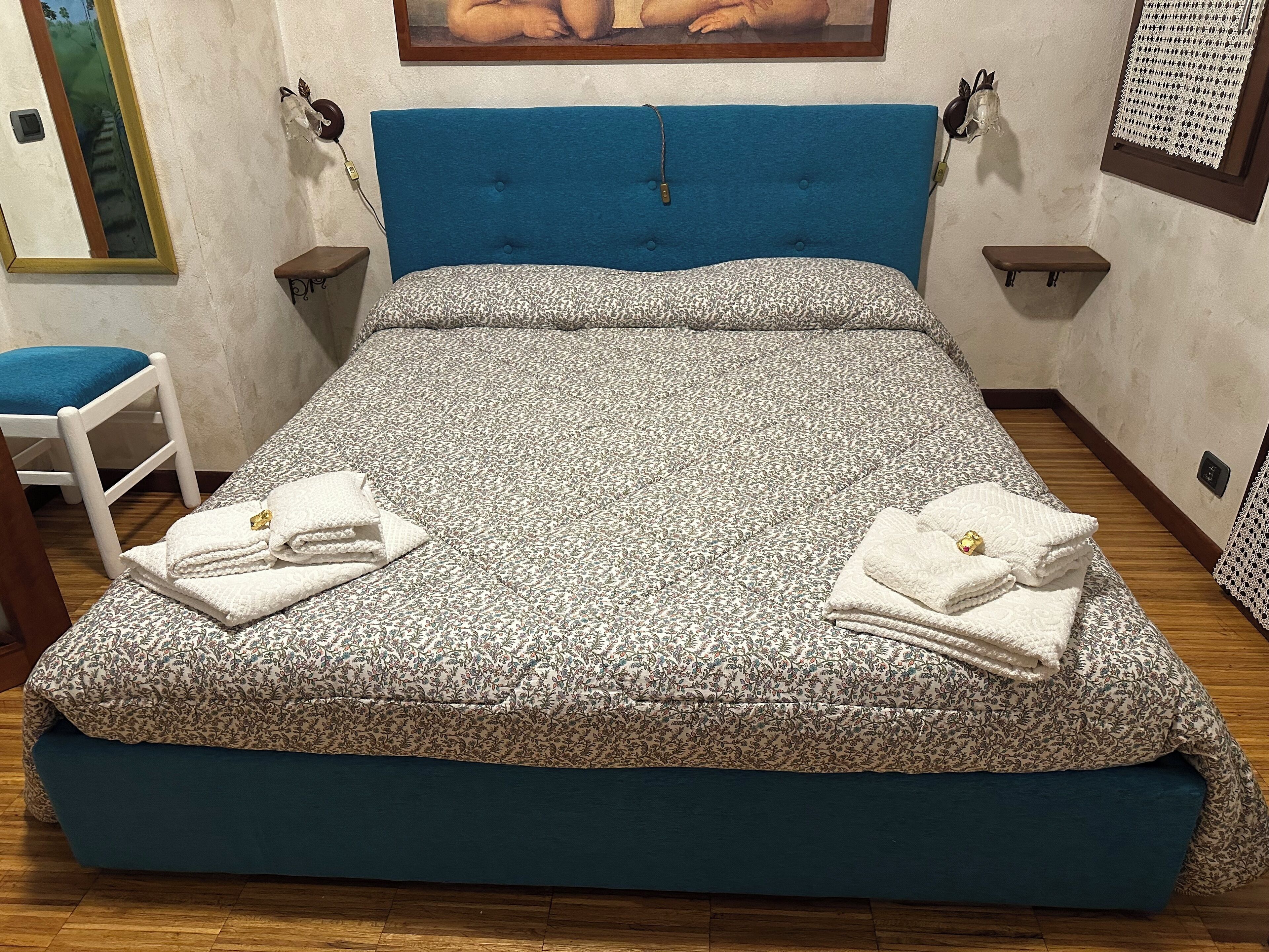 A neatly made bed with a floral-patterned bedspread and two folded towels on the foot of the bed.