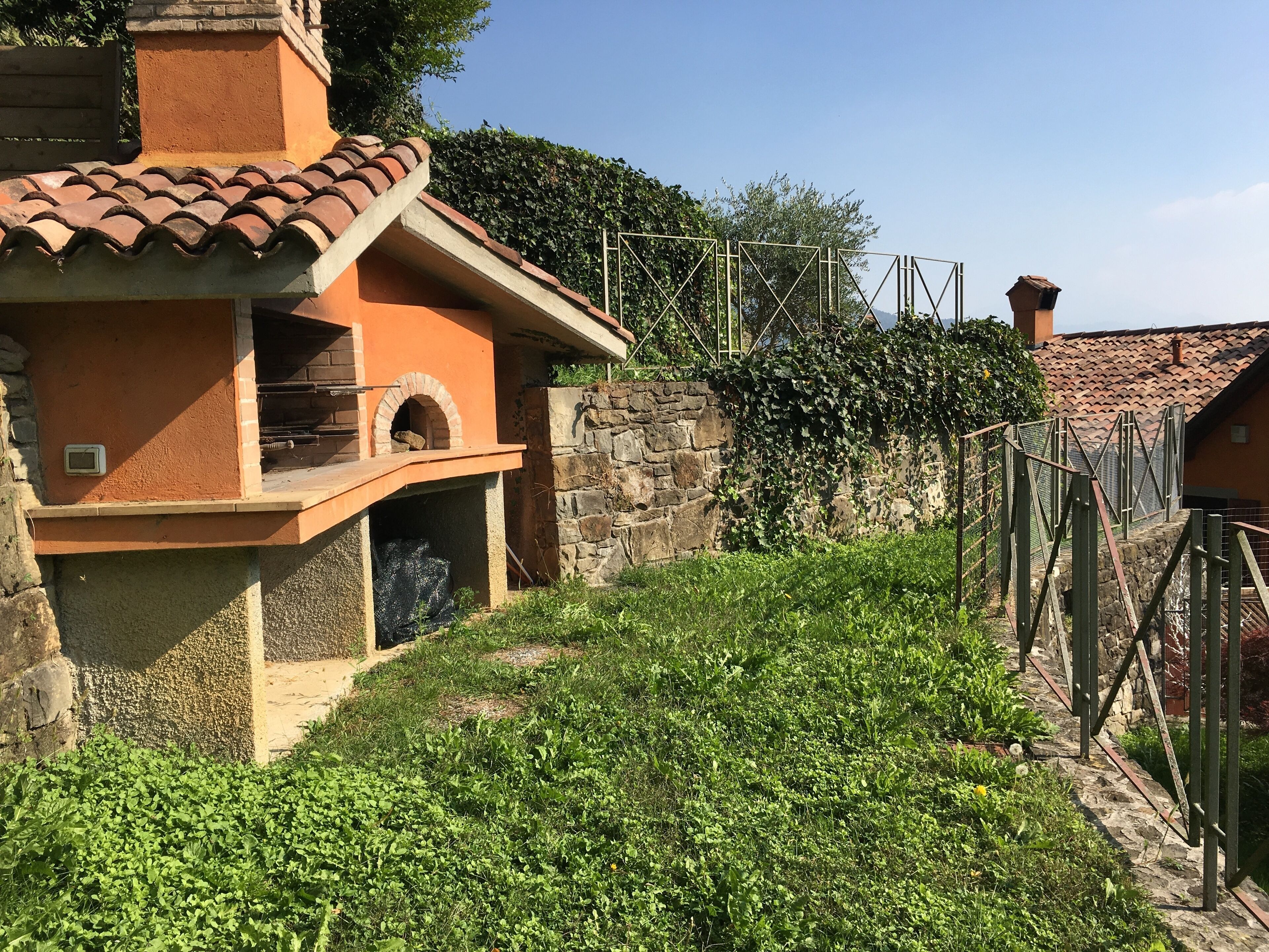 A rustic building with a tiled roof, a stone wall, and a metal fence.