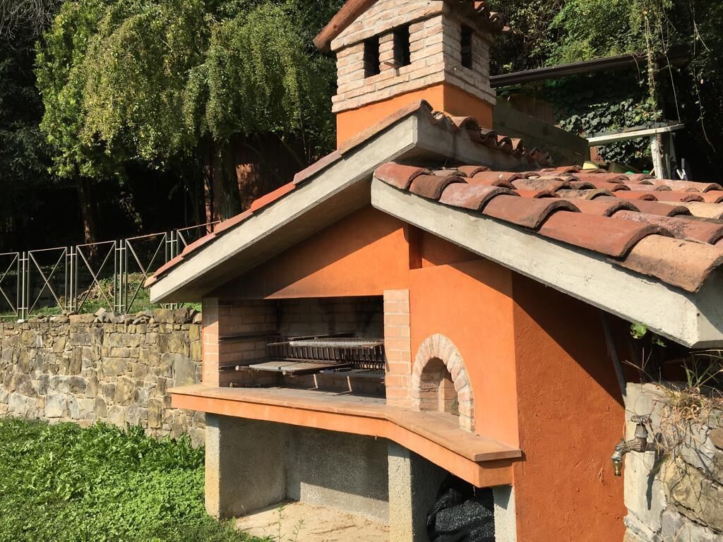 A brick-built outdoor kitchen with a chimney, a stone wall, and a metal fence in the background.