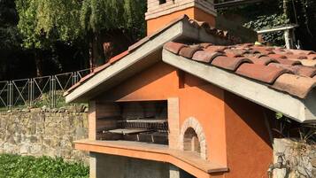 A brick-built outdoor kitchen with a chimney, a stone wall, and a metal fence in the background.