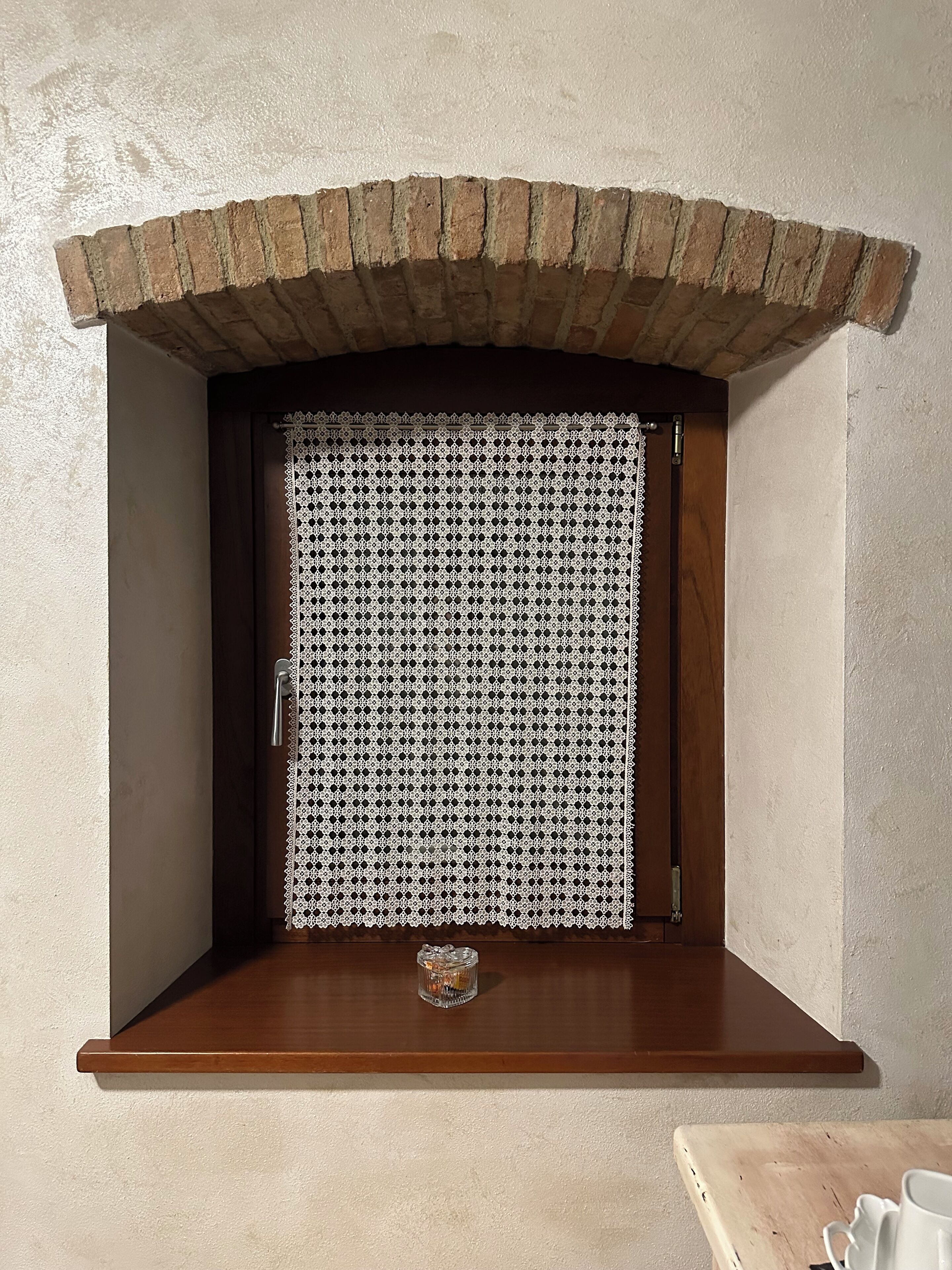 A brick fireplace with a decorative white lace door, a small shelf below, and a wooden table to the right.