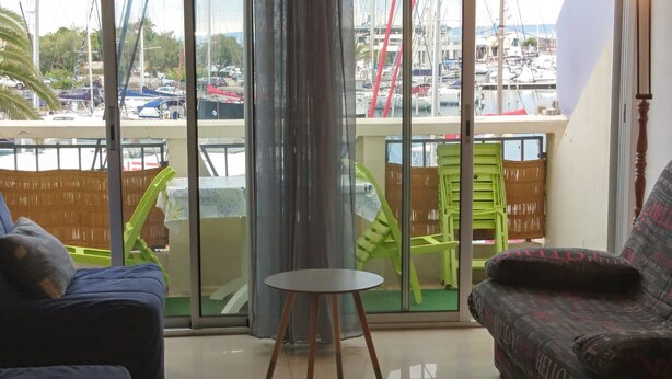 A modern living room with a view of a marina, featuring two sofas, a small round table, and a large sliding glass door. - Charming studio in enjoyable La Grande-Motte with WiFi (La Grande-Motte)