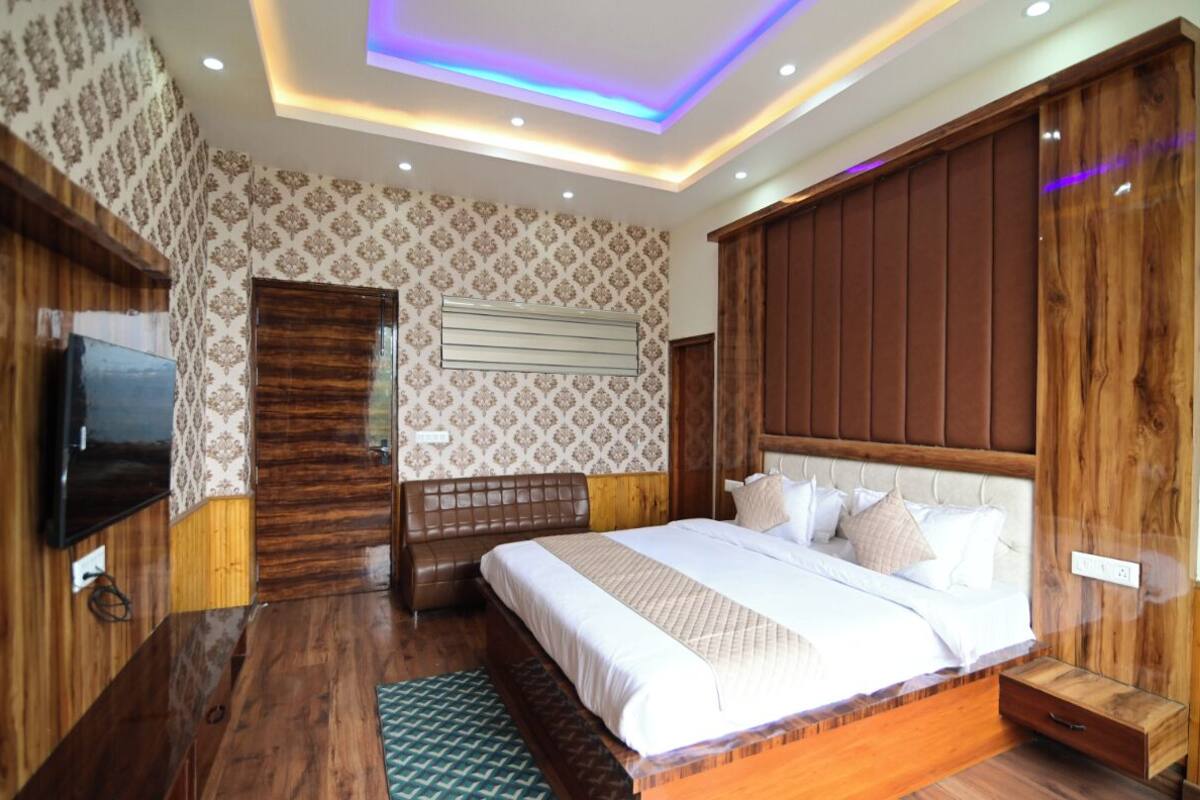 A bedroom with a wooden headboard, a large bed with multiple pillows, a flat-screen TV mounted on the wall, and a patterned wallpaper.