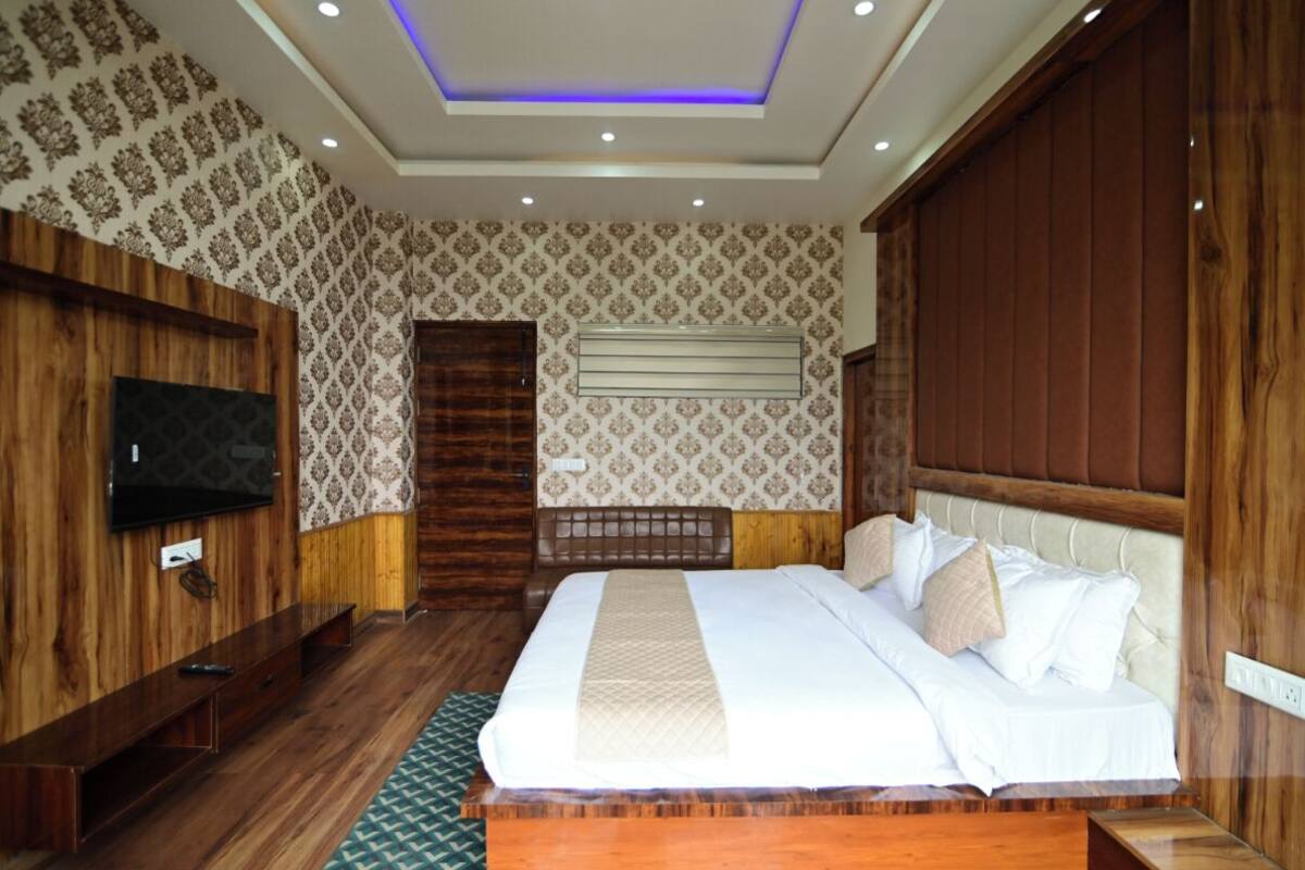 A hotel room with a large bed, wooden paneling, a flat-screen TV, and a patterned wallpaper.