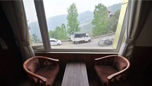 Una habitación con dos sillas de madera y una mesita, una ventana con vistas a una carretera y montañas.
