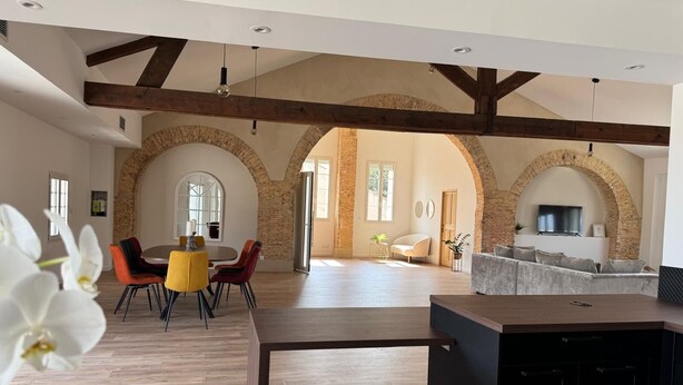 A spacious living area with high ceilings, exposed wooden beams, and a stone archway.