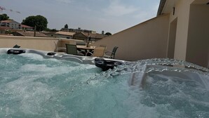 A hot tub area with a table and chairs, surrounded by a beige wall and a clear sky.