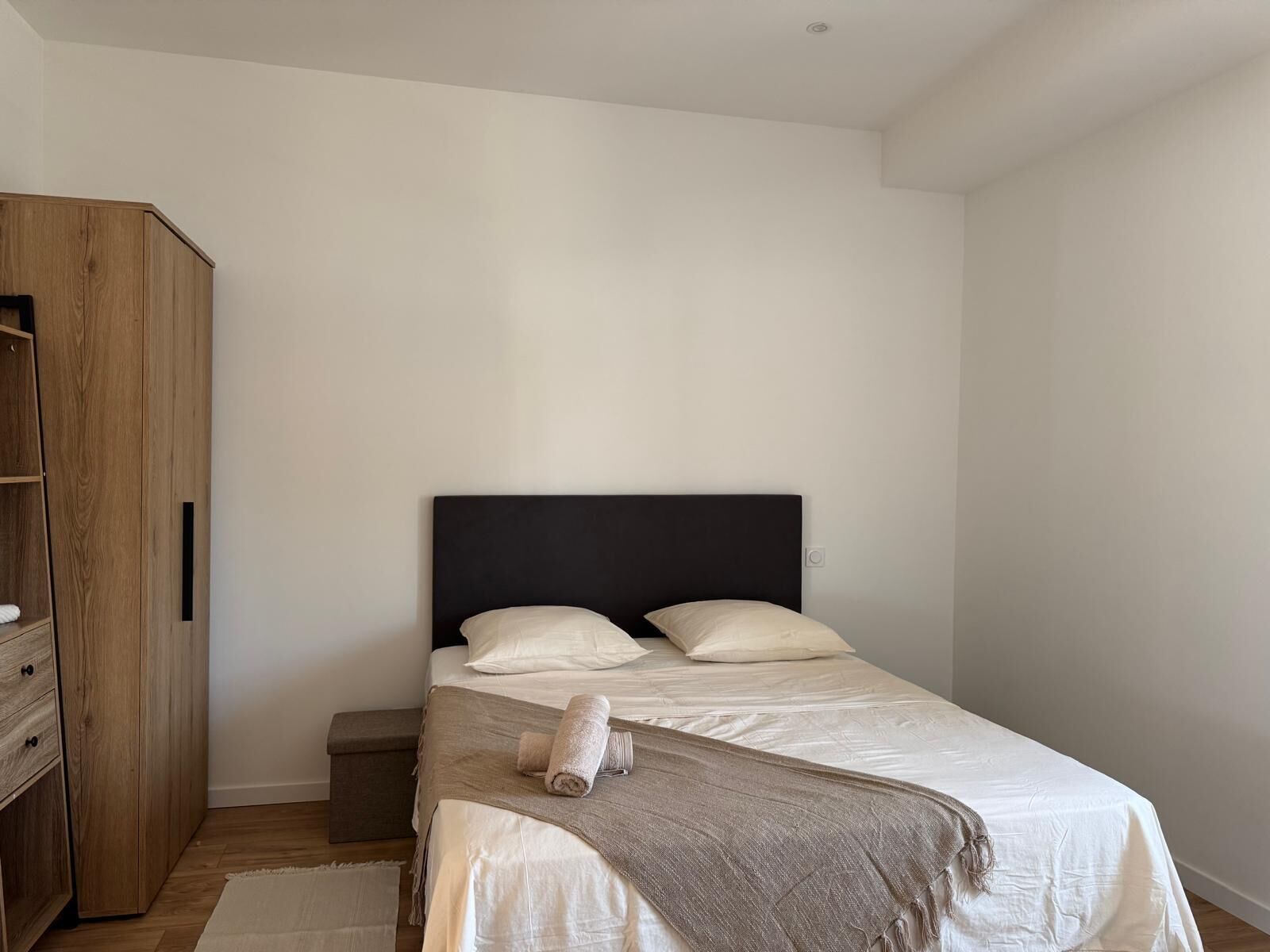 A bedroom with a bed, a wooden wardrobe, and a small bedside table.
