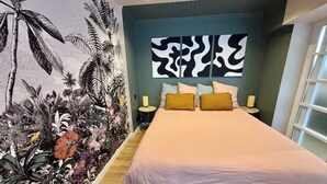 A bedroom with a bed, two bedside tables, a wall with a tropical mural, and a window. - House + garage in the heart of ORANGE (Orange)