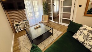 A modern living room with a flat-screen TV, a sofa, a coffee table, and a sliding glass door leading to a balcony. - House + garage in the heart of ORANGE (Orange)