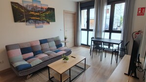 A living room with a sofa, a coffee table, a dining table with chairs, a potted plant, and a painting on the wall. - Sella Rooms (Arriondas)