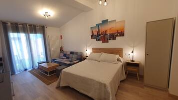 Een slaapkamer met een bed, een bank, een nachtkastje, een lamp, een brandblusser en een stadsgezichtschilderij aan de muur.