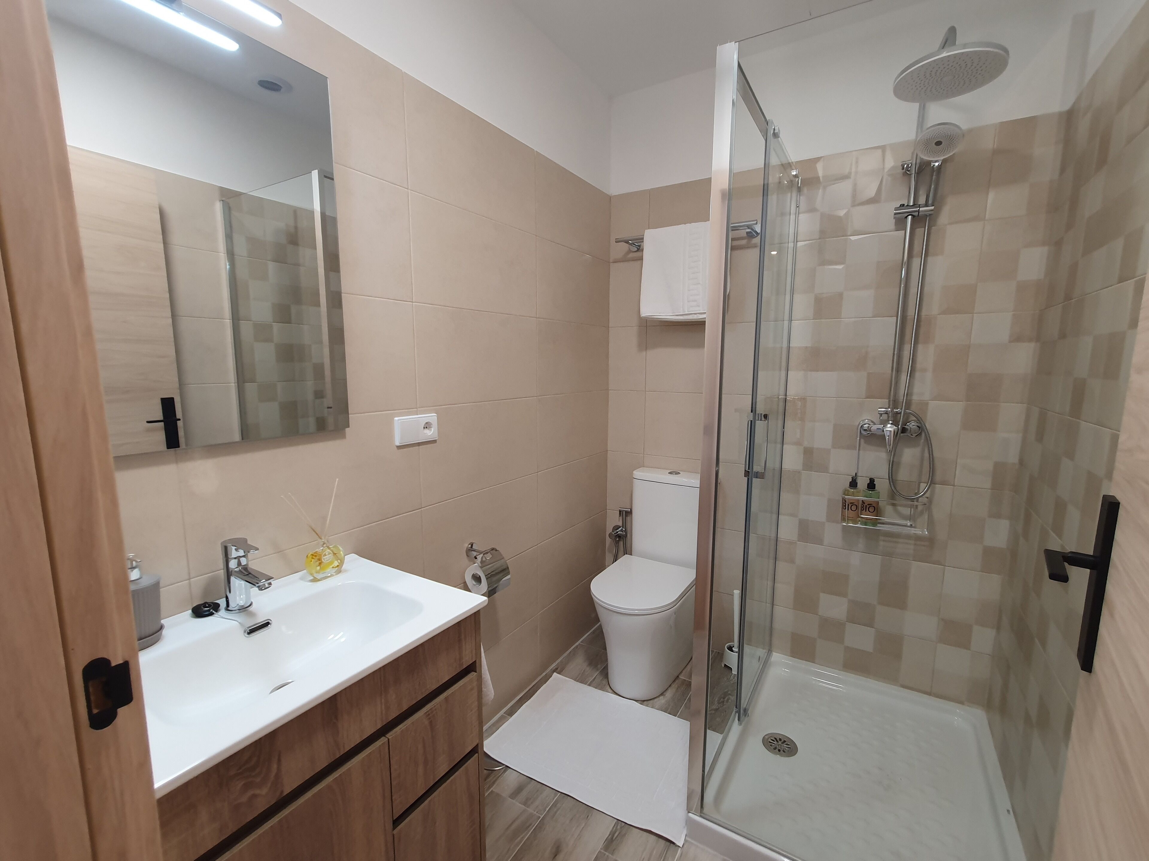 Een badkamer met een douche met glazen wand, een toilet, een wastafel met spiegel en een houten kast.