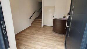 A hallway with wooden flooring, a staircase, a dark door, and a small cabinet with a plant. - Sella Rooms (Arriondas)