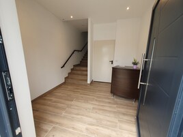Un pasillo con suelo de madera, una escalera, una puerta oscura y un mueble pequeño con una planta.