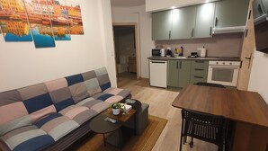 A compact living space with a sofa, a small dining table, a kitchen area with a microwave, a dishwasher, and cabinets. - Sella Rooms (Arriondas)