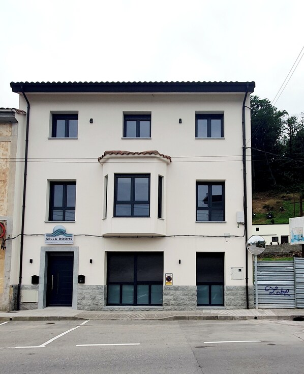 Il s’agit d’un bâtiment à deux étages, sur lequel on peut lire une enseigne indiquant « Sella Rooms », ce qui laisse supposer qu’il s’agit d’un hôtel. On y trouve trois portes de garage, une petite entrée avec une porte et un parking situé à l’avant.