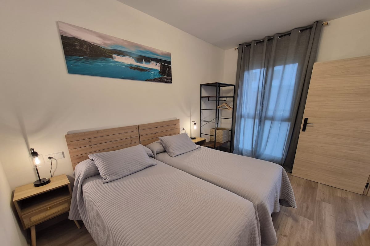 Een slaapkamer met twee bedden, een nachtkastje, een wandplank, een deur en een schilderij van een waterval.