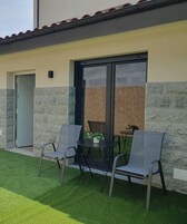 Un edificio de fachada de piedra, puerta corredera de vidrio y un pequeño patio con dos sillas y una mesa.