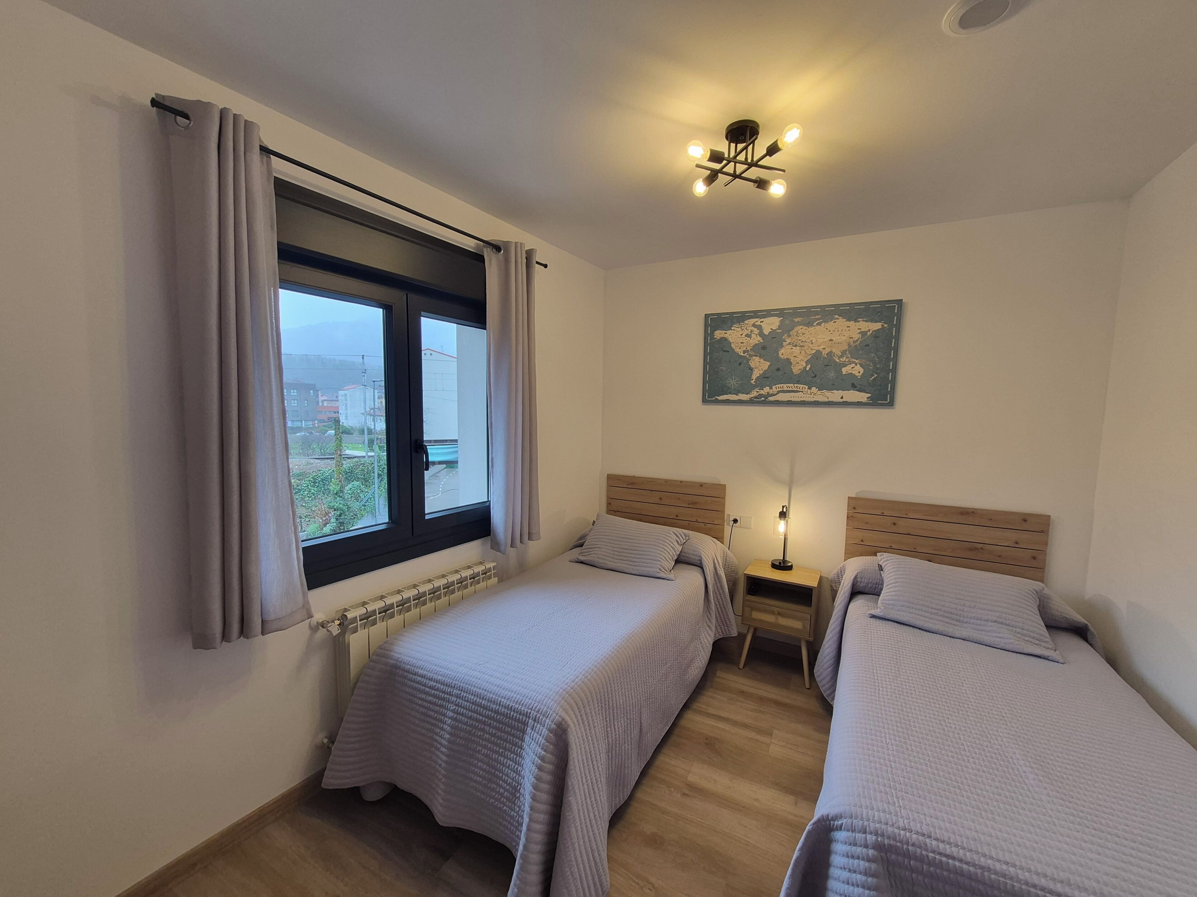 Habitación con dos camas, un mapa mundial en la pared, un radiador y una ventana con cortinas.