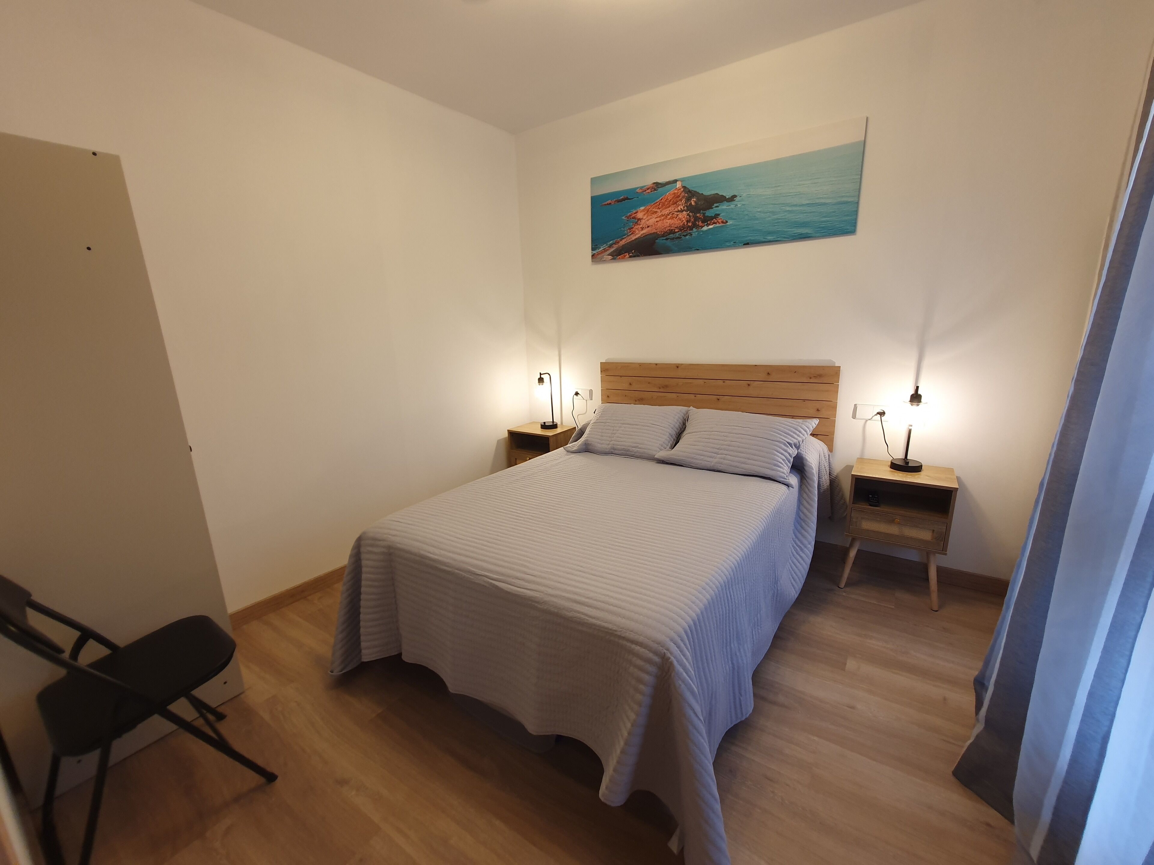 Une chambre à coucher avec un lit, deux tables de chevet, une chaise, un tableau au mur et un plancher en bois.