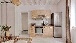 A modern kitchen with wooden cabinets, a stainless steel refrigerator, and a built-in oven. There is a small dining area with a table and chairs.