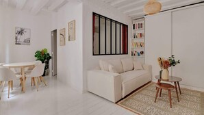 A modern living room with a white sofa, a dining table with chairs, a bookshelf, and a hanging light fixture.