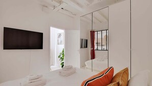 A modern hotel room with a large bed, a flat-screen TV mounted on the wall, a large mirror, and a view of the outside through a door.