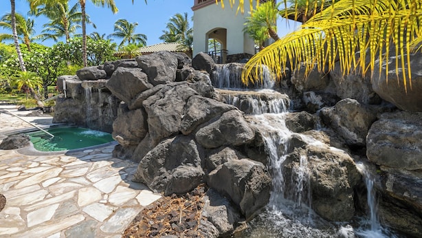 Un resort tropical con una cascada, piscina de piedra y palmeras.