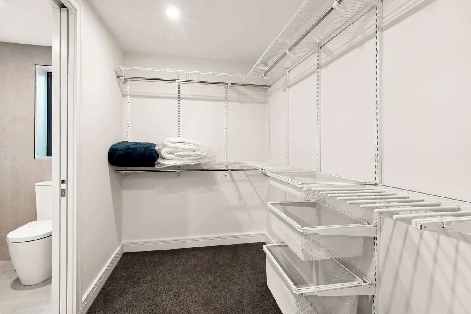 A walk-in closet with open shelving, a small shelf with folded towels, and a trash can.