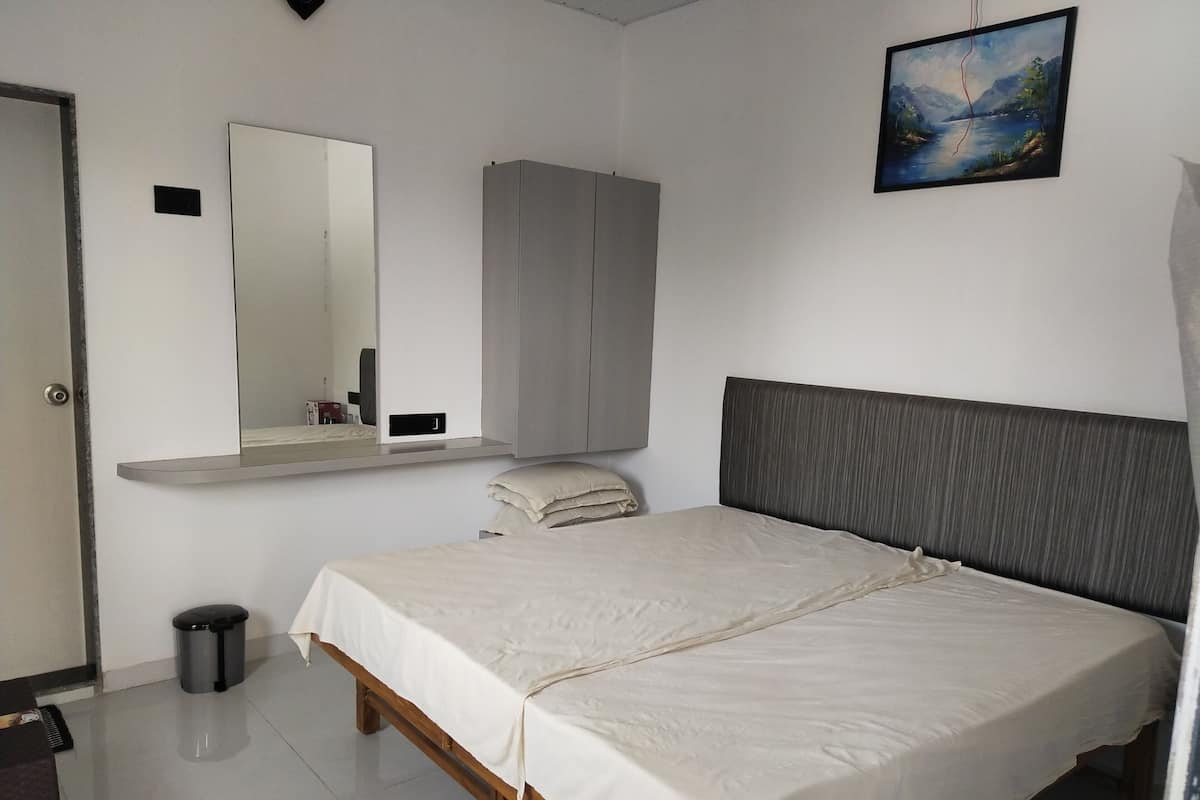 A bedroom with a bed, a mirror, a wardrobe, a picture on the wall, and a trash bin.
