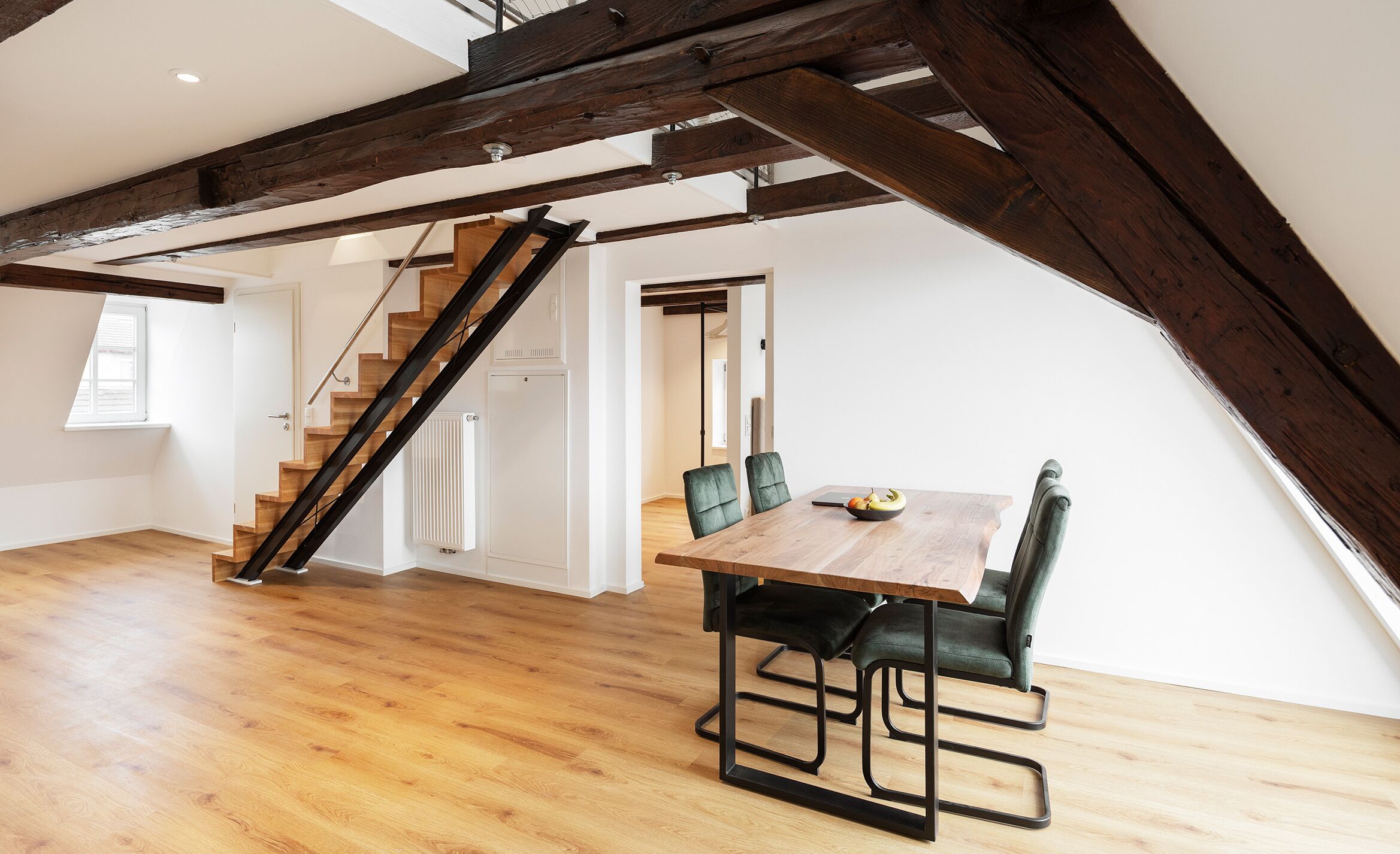 Ein geräumiges Loft mit Holzboden, einem Esstisch mit Stühlen und einer Treppe mit freiliegenden Balken.