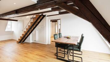 Ein geräumiges Loft mit Holzboden, einem Esstisch mit Stühlen und einer Treppe mit freiliegenden Balken.