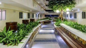 A hotel corridor with a central pathway, benches, and potted plants on either side. - Room-peaceful City View Condo for Rent i (Quezon City)