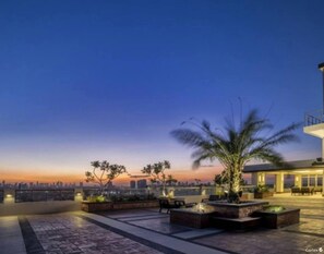 Une terrasse sur le toit, aménagée avec des espaces pour s’asseoir, des jardinières et offrant une vue sur les toits de la ville au crépuscule.