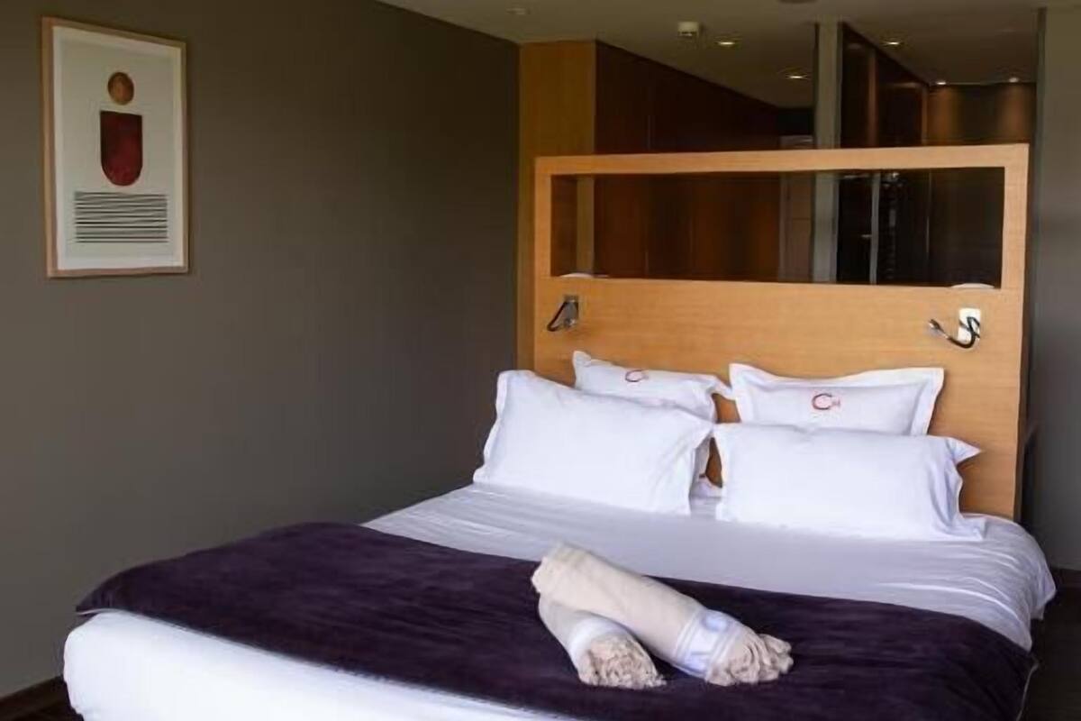 A neatly made bed with white and purple bedding, a wooden headboard, and a framed picture on the wall.