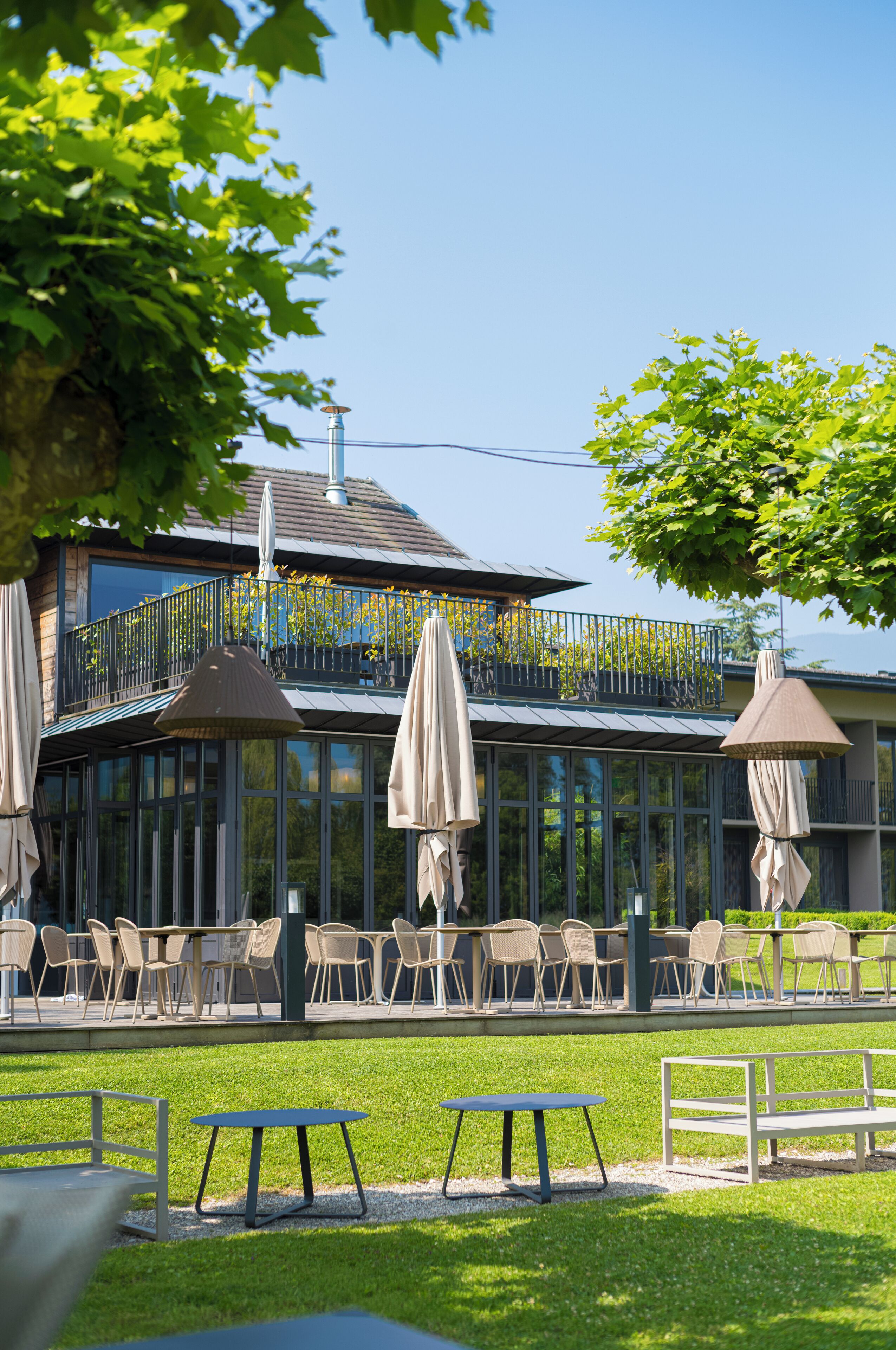 An outdoor seating area with tables and chairs, umbrellas, and a building with a balcony in the background.