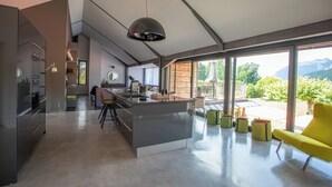 A modern kitchen with a central island, large windows, and a view of the outdoors.
