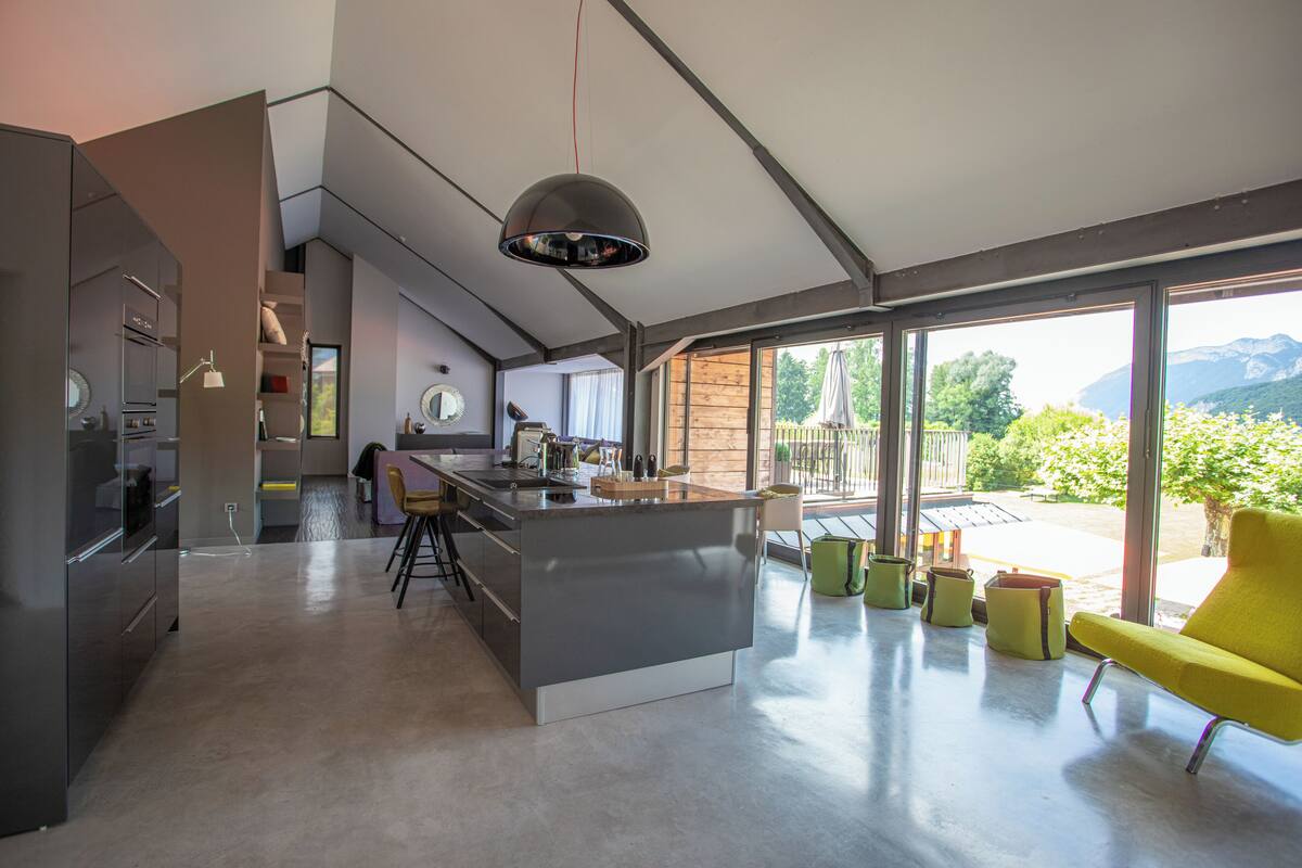 A modern kitchen with a central island, large windows, and a view of the outdoors.