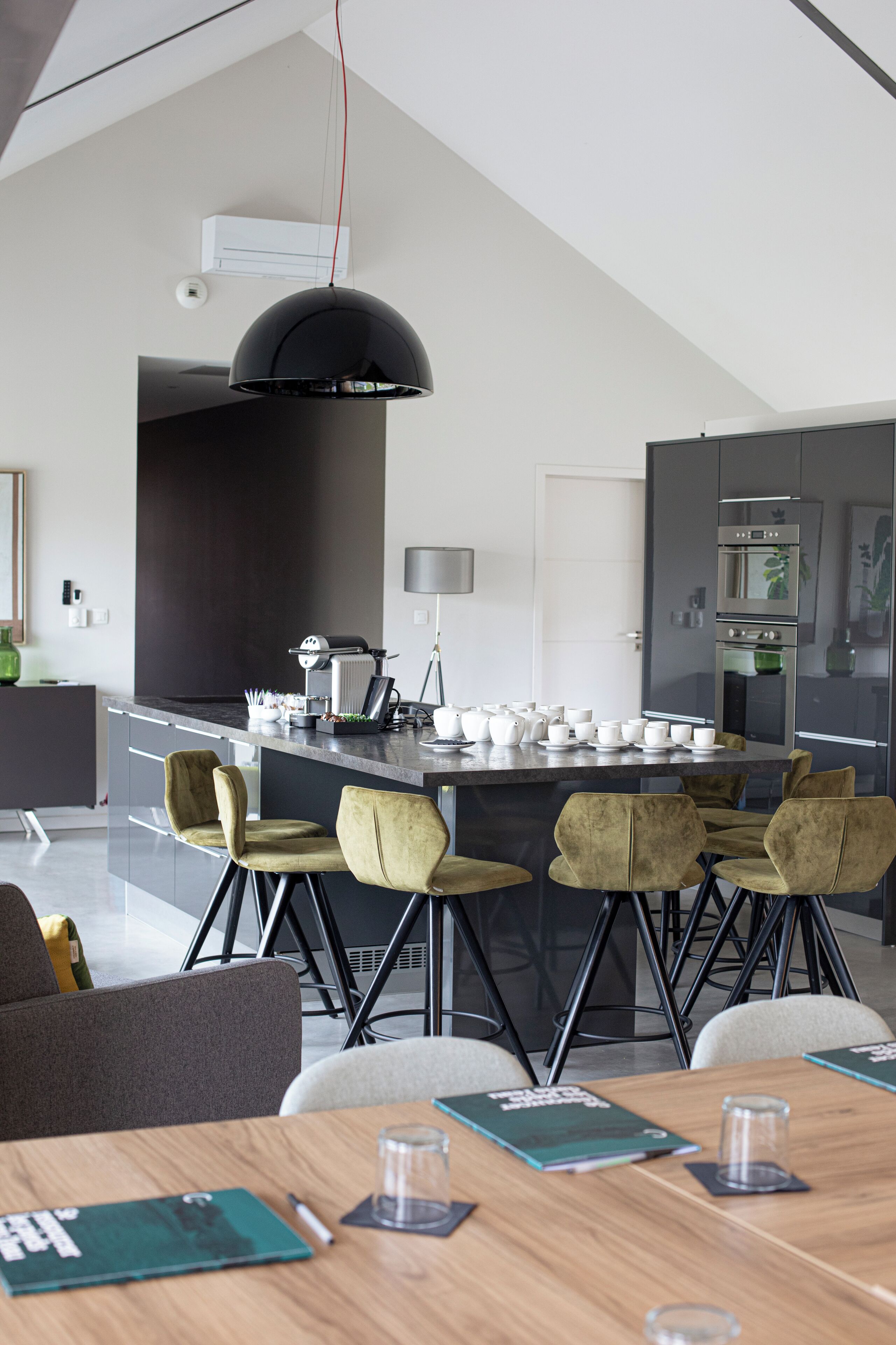 Una cocina moderna con una isla central, un área de comedor con una mesa y sillas de madera, y una lámpara colgante grande.