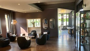 A modern lounge area with dark sofas, a glass cabinet with bottles, and a view of the outdoors through large windows.