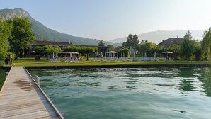 A wooden dock leading to a calm lake with lounge chairs and umbrellas on the grassy area.