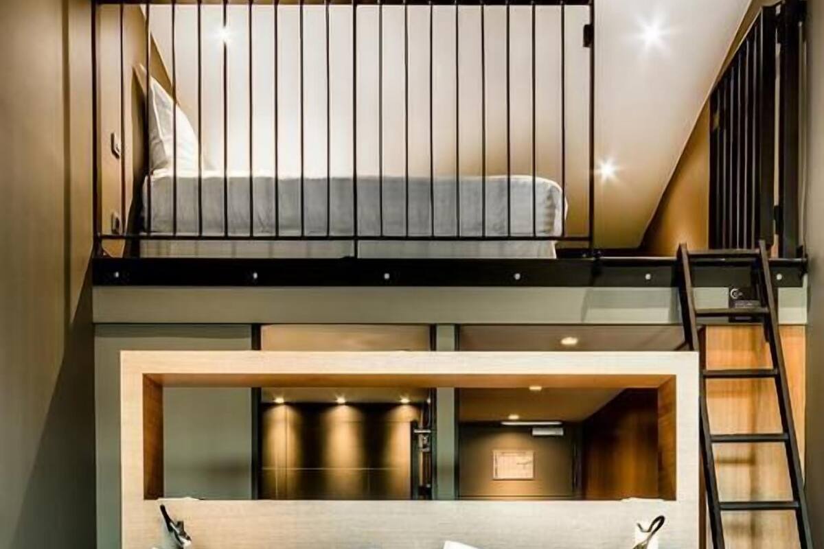 A hotel room with a bunk bed, a desk, and a ladder.