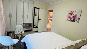 A bedroom with a bed, a desk, and a chair. There is a door leading to another room.