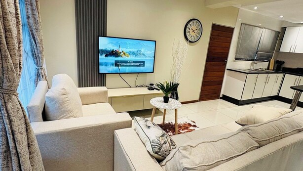 A modern living room with a sofa, a TV, and a kitchen area in the background.