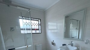 A modern bathroom with a glass shower enclosure, a white toilet, a white sink with a vessel basin, and a large mirror above the sink.
