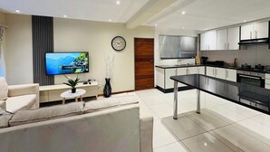A modern living room with a flat-screen TV, a sofa, a coffee table, and a dining area with a black table and chairs.