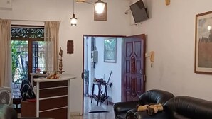 Un salon avec un canapé, une table basse et un téléviseur fixé au mur. Il y a une fenêtre avec des rideaux et une porte qui donne sur une autre pièce.